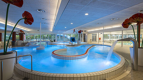 Recreatiebad met watervallen en grote decoratieve klaprozen naast het zwembad